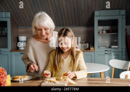 Happy senior woman making breakfast with her granddaughter in kitchen at home Stock Photo