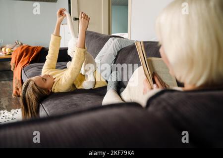 Grey mature woman reading book while spending time with her granddaughter at home Stock Photo
