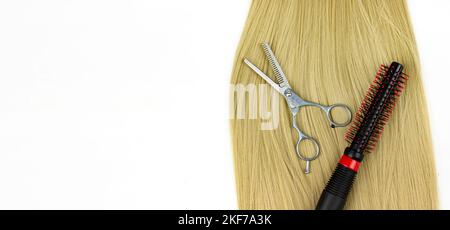 Curling brush on blonde hair with scissors on white background. Round brushing combs long blond hair closeup Stock Photo