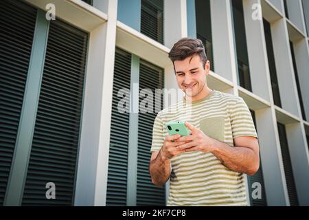 Happy teenager male smiling and typing on a smart phone using a social media app outdoors. Slowmotion 4k. Young man having fun texting messages on a Stock Photo