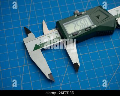 Photo of a digital vernier caliper with centimeters and millimeters on a blue background cutting mat Stock Photo