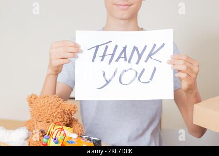 Thank you for donation. Volunteers collecting donations for charity. Teenage boy holding paper card with message Thank you over cardboard boxes full Stock Photo