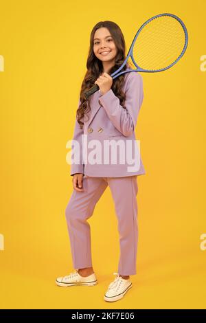 Fashion teenage tennis player girl in trendy suit hold tennis racket over isolated yellow background. Tennis school. Stock Photo