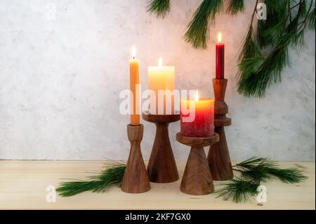 Four candles on wooden stands, all are lit for the fourth Advent, pine branch decoration, light wooden board and rustic plaster background, copy space Stock Photo