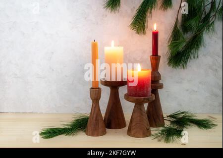 Four candles on wooden stands, three are lit for the third Advent, pine branch decoration, light wooden board and rustic plaster background, copy spac Stock Photo