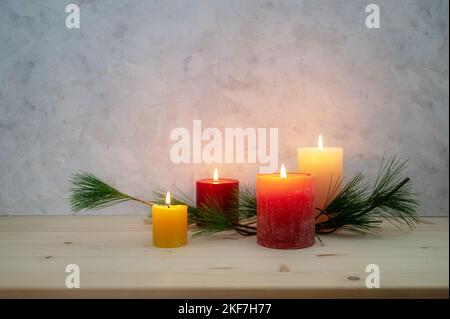 Four candles lit for the fourth Advent, pine branch as a simple, minimal decoration on a light wooden board against a rustic plaster wall, large copy Stock Photo