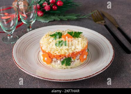 Layered salad with chicken, potatoes, carrots and cheese on a round plate on brown background Stock Photo