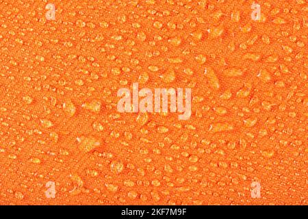 Waterproof clothing or upholstered furniture made from waterproof textiles. Drops of water on orange textiles with water-repellent properties. Stock Photo