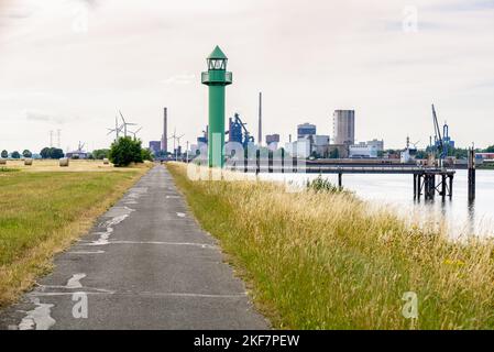 Lighthouse along a paved path on the bank of the river Weser in Bremen, Germany. Industrial plants and warehouse are visible in background. Stock Photo