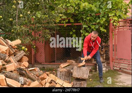 A man is chopping firewood for the winter, a young man is splitting a log with an axe. pieces of the log fly apart. selective focusing. Stock Photo