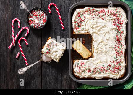 christmas vanilla sheet cake with whipped buttercream frosting garnished with sprinkles in baking dish on dark wooden table with candy canes, horizont Stock Photo