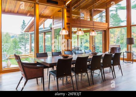 Wooden dining table with rawhide armchairs, black leather chairs and illuminated industrial style copper with frosted glass pendant lighting fixtures. Stock Photo