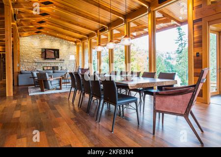 Wooden dining table with rawhide armchairs, black leather chairs and illuminated industrial style copper with frosted glass pendant lighting fixtures. Stock Photo