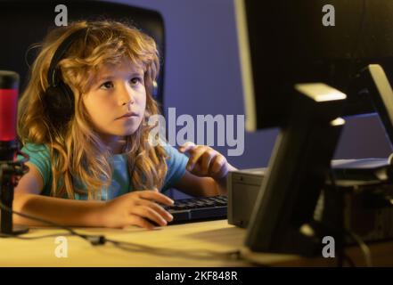 Child plays a video game on the pc computer screen. Portrait of cute child while typing on keyboard. Gamer play computer games. Neon lighting. Stock Photo