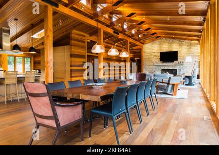 Wooden dining table with rawhide armchairs, black leather chairs and illuminated industrial style copper with frosted glass pendant lighting fixtures. Stock Photo