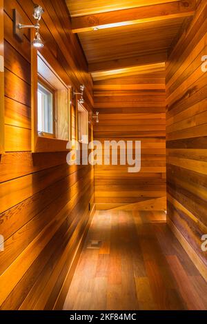 Illuminated upstairs hallway with Ipe wood floor cedar plank walls and ceiling inside luxurious stained cedar and timber wood home. Stock Photo