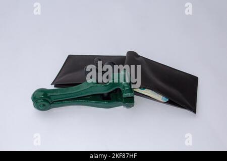 Image of a clamp that keeps a wallet closed and blocked from which banknotes come out. Reference to the global crisis, rising prices and savings Stock Photo