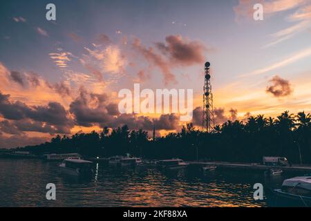 Wide-angle shot of a stunning sunset sky over the an island jetty full of small passenger boats, motorboats, and launches, with silhouette of palm tre Stock Photo