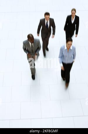 Off to work they go. High angle shot of a group of businesspeople walking through the office lobby. Stock Photo