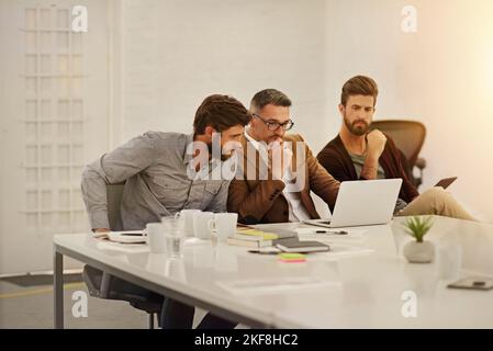 Putting their heads together. three businessmen looking at a laptop in the boardroom. Stock Photo