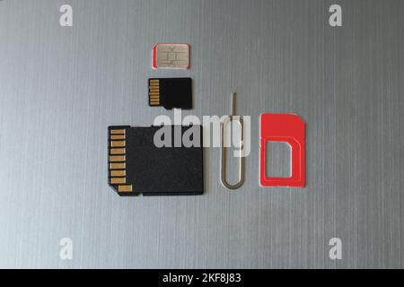 SIM card and paper clip to open the SIM card slot and the memory card are on a gray steel background Stock Photo