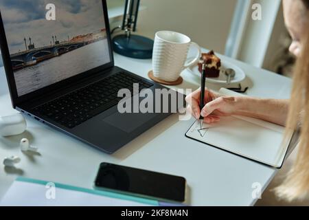 Home office workplace with laptop. Woman working remotely from home, using laptop. Creative freelancer drawing in notebook Stock Photo