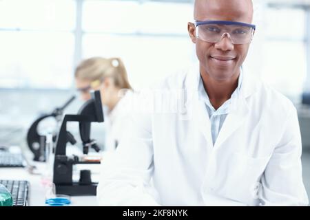 The science guy. Portrait of a smiling young chemist in the lab with a female coworker in the background. Stock Photo
