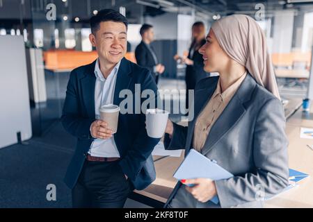 Two happy multiracial colleagues talking and drinking coffee during break time in office Stock Photo