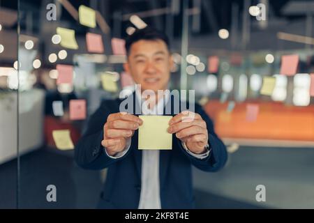 Asian Businessman showing empty sticky notes while standing in modern office Stock Photo