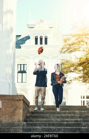 Students, walking and talking on education, study and happy on college or university campus outdoor. Black man and woman with ball, conversation and Stock Photo