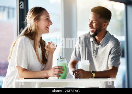 Couple, drink and happy with talking, date and enjoy in shop, cafe or store with smile, happy and romance. Interracial man, woman or friends in funny Stock Photo