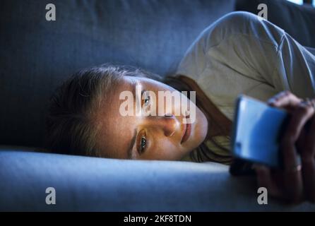 Phone, night and sad woman relaxing on sofa in living room scrolling on social media after a break up. Depression, upset and girl on couch in lounge Stock Photo