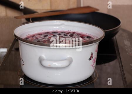 homemade fruit compote with cherry boils on the stove in the kitchen in a white saucepan, fruit compote in a saucepan Stock Photo