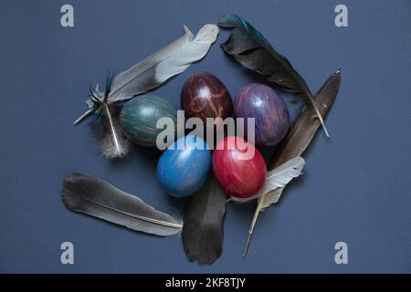 decorated chicken eggs with watercolor multi-colored paints and dove feathers on a blue background, easter prazdnik and culture Stock Photo