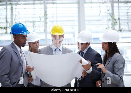 Making sure his design is perfect. A diverse group of serious-looking architects looking over blueprints together. Stock Photo