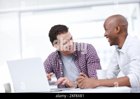 They have a lot of fun working together. Two businessmen working on a project while sitting together at a desk. Stock Photo