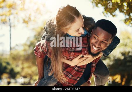 Love, piggy back and couple in park walking, smile and happy together, for bonding and outdoor. Romantic, interracial man and woman or loving on Stock Photo