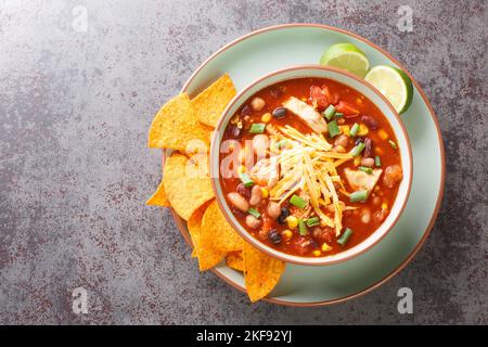 Chicken taco soup cooked in fragrant broth with beans, corn, tomatoes served with lime and tortilla chips close-up in a plate on the table. Horizontal Stock Photo