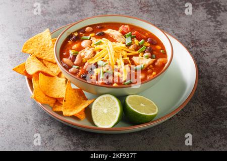 Chicken Taco Soup with black bean, corn kernels, tomatoes topped with cheddar cheese in green bowl on a table, horizontal Stock Photo