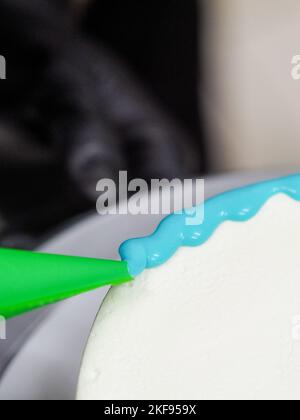 pastry chef cake designer decorating turquoise blue white frosted cheesecake in kitchen with piping bag Stock Photo