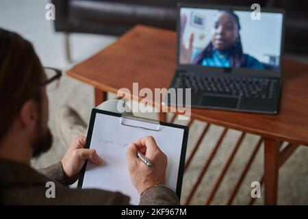 Close-up of professional psychologist making notes in card while talking to patient online on laptop at office Stock Photo