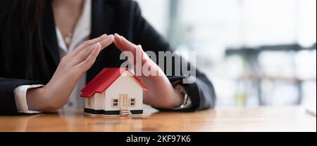 Wooden toy house protected by hands with copy space. Home insurance concept. banner ratio Stock Photo