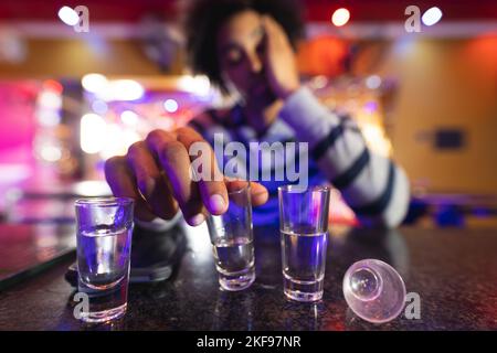 Drunk african american man sitting at the bar with shot glasses, selective focus Stock Photo