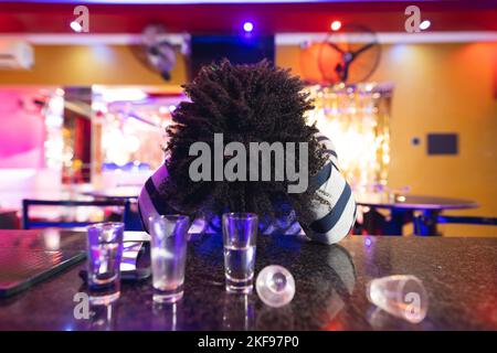 Drunk african american man sitting at the bar with head down and empty shot glasses Stock Photo
