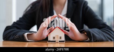 Wooden toy house protected by hands. Home insurance concept. banner ratio Stock Photo