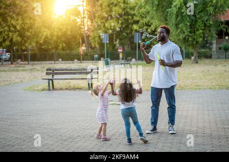 Parent playing the bubble game with interracial children outdoors Stock Photo