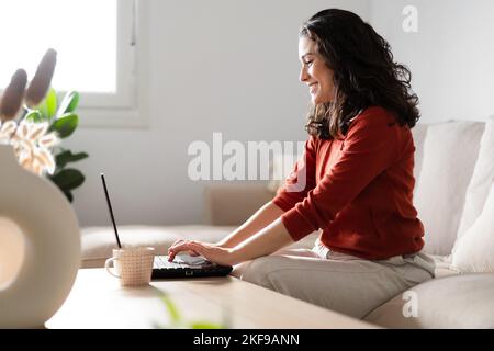 Happy young woman using laptop sitting on a couch at home. Working from home concept Stock Photo