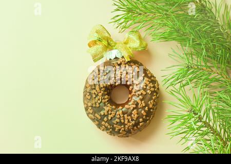 chocolate donut with golden bow like christmas ball near fir tree. top view from above. single glazed donut with chips. ring small fried cake Stock Photo
