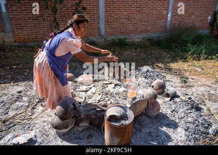 Making red clay pottery.  The potter starts to prepare to build a fire to fire pottery in San Marcos Tlapazola, Mexico.  She does not use a convention Stock Photo