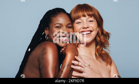Happy women with different skin tones smiling at the camera while standing together. Two body confident young women embracing their natural beauty. Ch Stock Photo